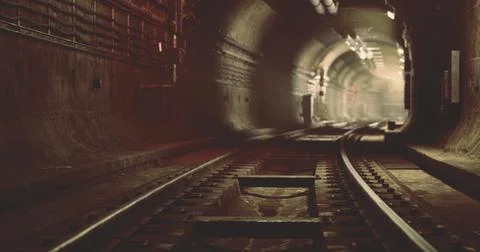 Train tracks leading into a dimly lit tunnel in an underground railway system Illustrazione stock