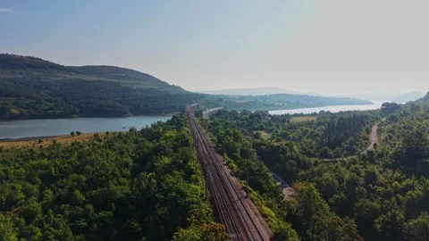 Train tracks run along a river and hills in the countryside Stock Footage 340381821