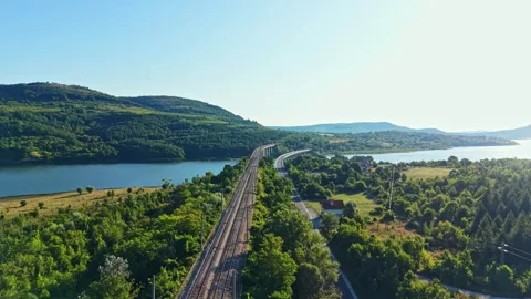 Train tracks run along a river with hills in the background during a sunny day Stock Footage 341698187