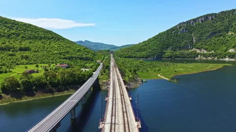 Train tracks run along a river with green hills in the background near a small Stock Footage 342480374