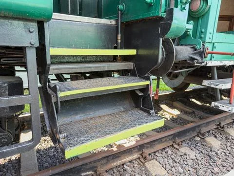 Train undercarriage featuring rustic metal steps near tracks, dark green tr.. Stock Photos
