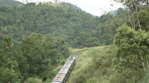 Train winding through lush green forested hills on railway curve, Sri Lanka Stock Footage 331143384