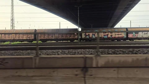 Train window view of railway tracks under an overpass bridge and freight ca.. Vídeos de archivo 344673195
