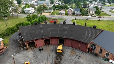 Train Yard With Multiple Tracks and Roundhouse in Open Area Near Town Stock Photos
