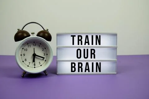 Train Your Brain text on LED lightbox with alarm clock on purple background 写真素材