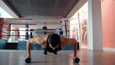 A trained, motivated man does push-ups with his hands on dumbbells in a gym Stock Footage 156697270