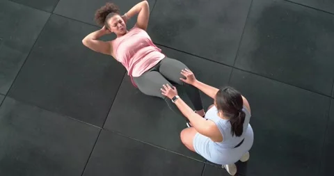 Trainer anchoring client feet on rubber mat while client performing sit-ups and Stock Footage 344224374