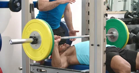 Trainer assisting man bench pressing barbells at a gym Vídeos de archivo 56212633