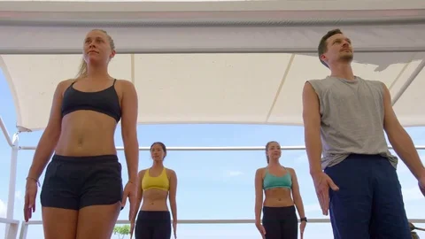 Trainer assisting people during practicing yoga exercise near the sea Stock Footage 74769207