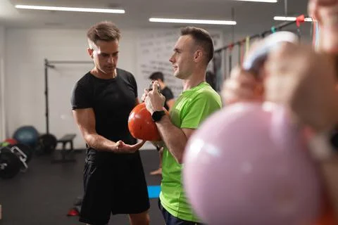 A trainer assists trainee performing squats with the kettlebell Stock Photos