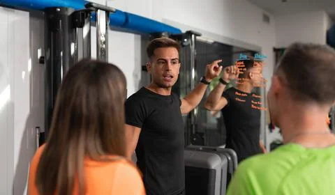 A trainer explains the upcoming exercise session to a young trainee couple Stock Photos