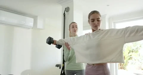 Trainer guiding client raising dumbbells adjusting elbow alignment for proper Stock Footage 344104754