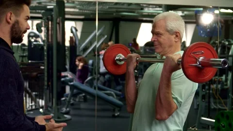 Trainer hands barbell to senior client in gym Stock Footage 311536590