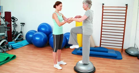 Trainer helping elderly client to use bosu ball Stock Footage 34254070