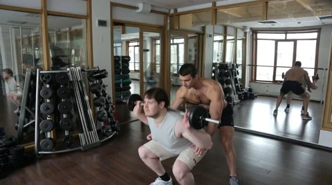 Trainer helps the beginner to do squats with barbell Stock Footage 64214711