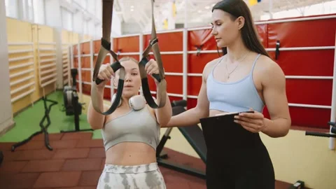 Trainer helps client with suspension exercise at gym during personal training se Stock Footage 344888390
