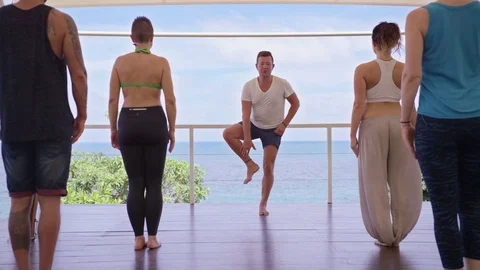 Trainer instructing a group of people performing tree pose near the sea Stock Footage 74772804