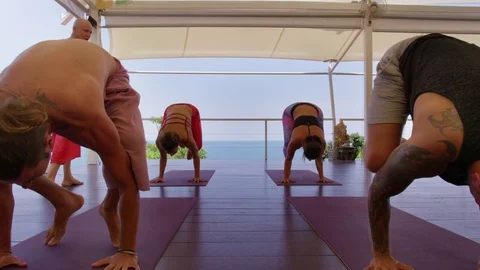 Trainer instructing a group of people performing yoga near the sea 스톡 동영상 74774097