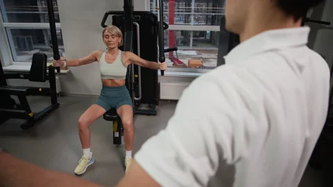 Trainer Instructing Woman Performing Exercise in Pec Deck Machine Stock Footage 328337491