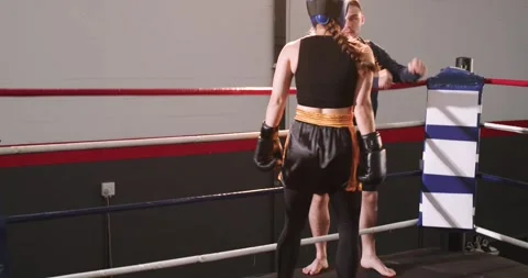 Trainer leaning over ropes giving cue, Female boxer inside ring adjusting guard Stock Footage 336366774