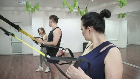 Trainer making squats with the trainees in TRX hall Stock Footage 73546115