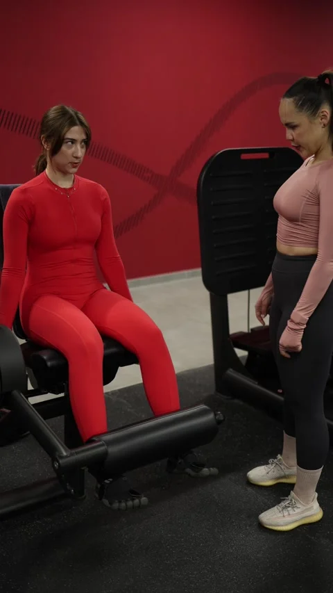 Trainer supervises leg extension exercise in gym Stock Footage 337956853