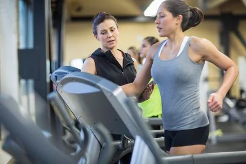 Trainer with tablet computer instructing woman exercising on treadmill in gym Stock Photos