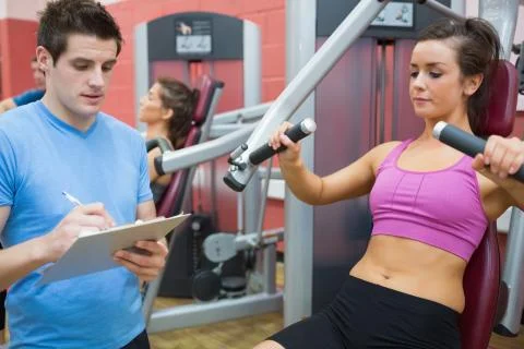 Trainer taking notes on client on weights machine Stock Photos