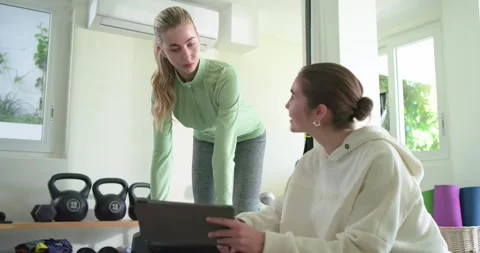 Trainer using tablet in home gym guiding female client doing dumbbell bench row Stock Footage 336658289