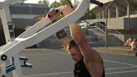 Training of a brutal man on outdoor simulators in the city sports park. Stock Footage 288333546