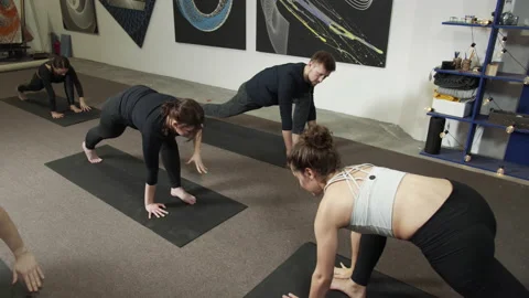 Training class practicing yoga in a small room with paintings on white wall Stock Footage 156241277