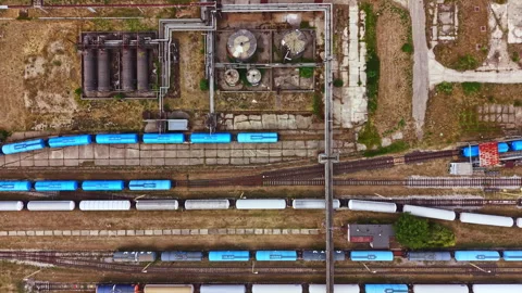 Trains are parked in a rail yard with buildings and pipelines visible during Stock Footage 344193950