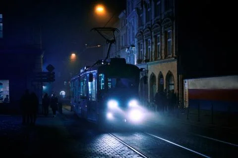 A tram going down the street in cold foggy night surrounded by people and old Stock Photos