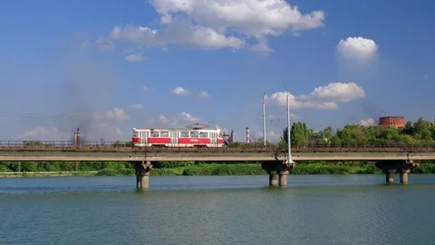 Tram moves along the bridge over the river on a background of industrial plant Stock Footage 112977009