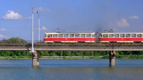Tram moves along the bridge over the river on a background of industrial plant Stock Footage 112977011