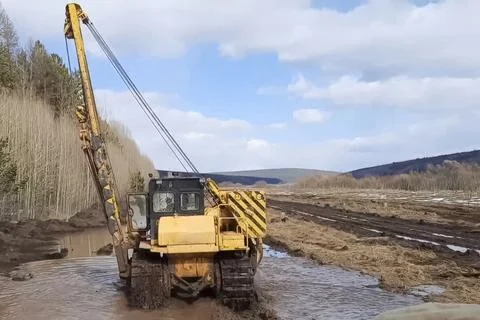 Tram paver drives through mud and puddle to the place where the pipe is laid. Stock Photos