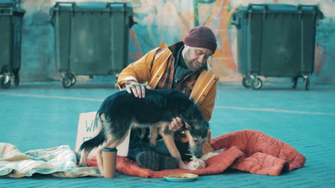 A tramp is petting his dog while sitting on the ground Vidéo 166575666
