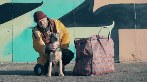 A tramp is stroking his dog with a massive bag next to them Vidéo 166956190
