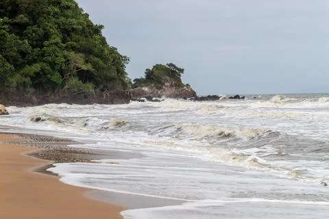 Tranquil beach scene featuring soft waves vibrant green cliffs under cloudy s Stock Photos