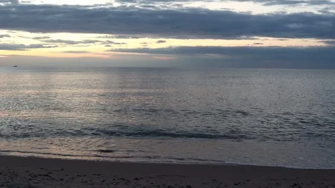 A tranquil beach scene with gentle waves under a cloudy evening sky at sunset, Stock Footage 313456500