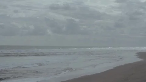 Tranquil Beach Scene with Gently Lapping Waves Under Overcast Sky Stock Footage 303340262