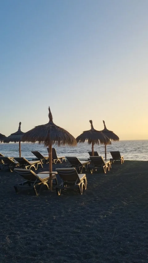 A tranquil beach scene in Tenerife with lounge chairs under thatched umbrellas Stock Footage 307635178