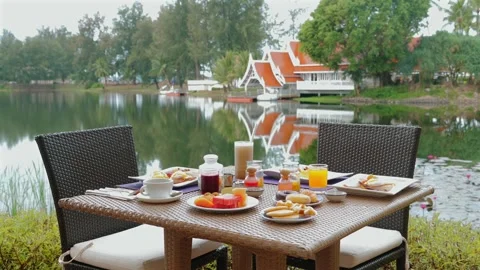 Tranquil breakfast setup at outdoor resort with view of serene lake Видео 260340394