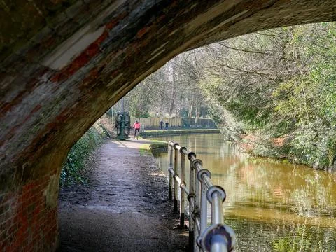 Tranquil canal path view under rustic brick bridge in daylight. Stock Photos