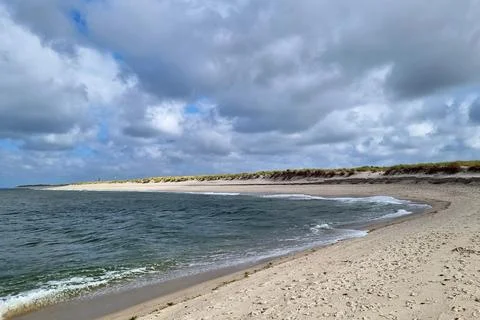 Tranquil Coastal Beach with Ocean Waves and Sandy Dunes on a Cloudy Day Stock Photos