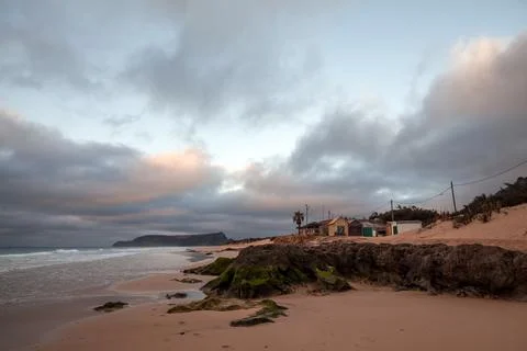 Tranquil coastal scene featuring a sandy beach, rugged rocks and wooden cabin Stock Photos
