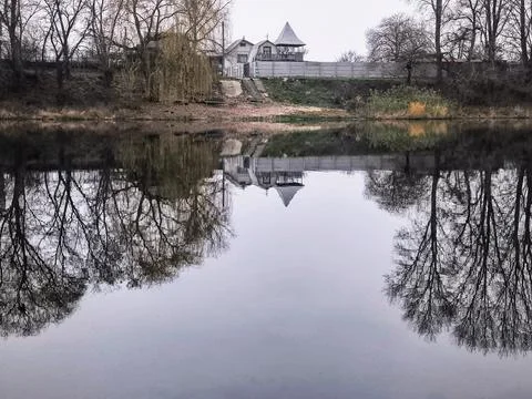 Tranquil lake with mirror-like reflections of leafless trees and cloudy sky.. Stock Photos