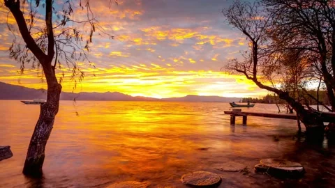 A tranquil lake scene at sunset with trees and distant mountains Stock Footage 312303092