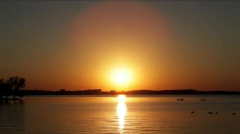 Tranquil lake at sunset, glowing orange, kayakers and ducks Stock Footage 12371555
