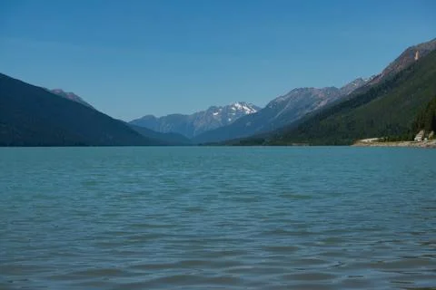 Tranquil lake surrounded by mountains under a clear blue sky on a sunny day Stock Photos